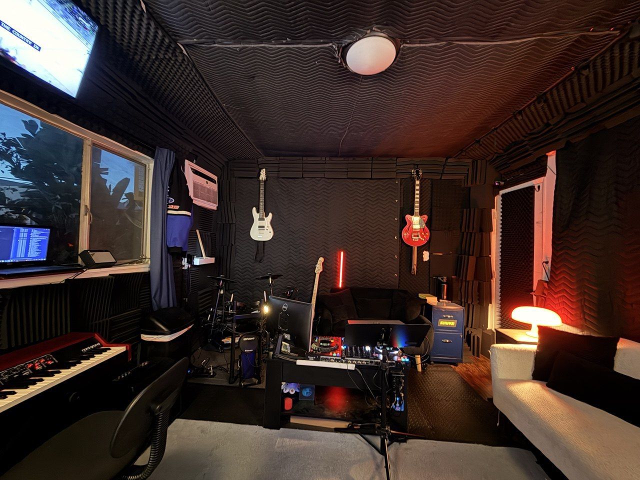 Guitar wall and back room, wall-mounted guitars, drums, red accent lighting, keyboard